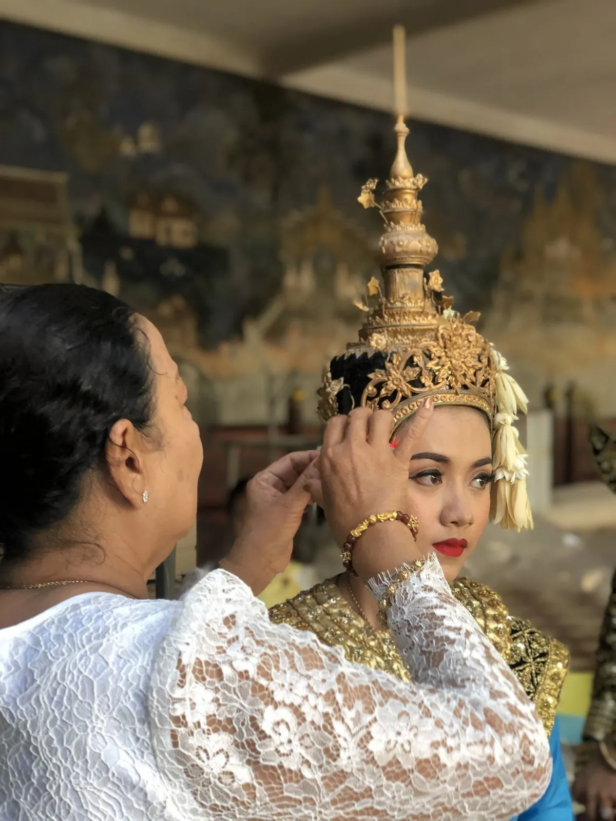 An older woman fitting a gold crown onto a classical dancer before a performance