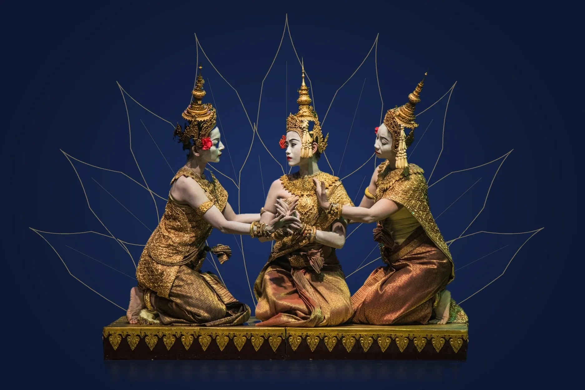 Three dancers in gold costume kneeling on a gilded dais before a drawn lotus