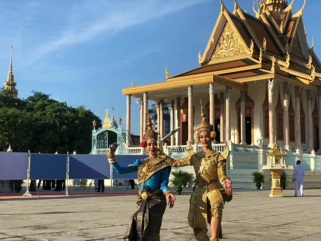 Two classical dancers in costume posing before a gilded royal pavilion under a clear sky